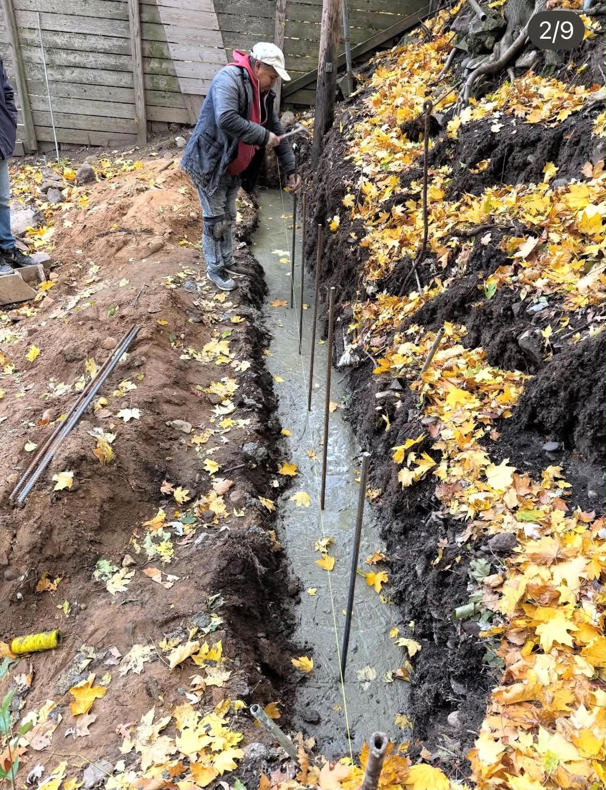 Crew pouring a reinforced concrete footing along a backyard retaining wall